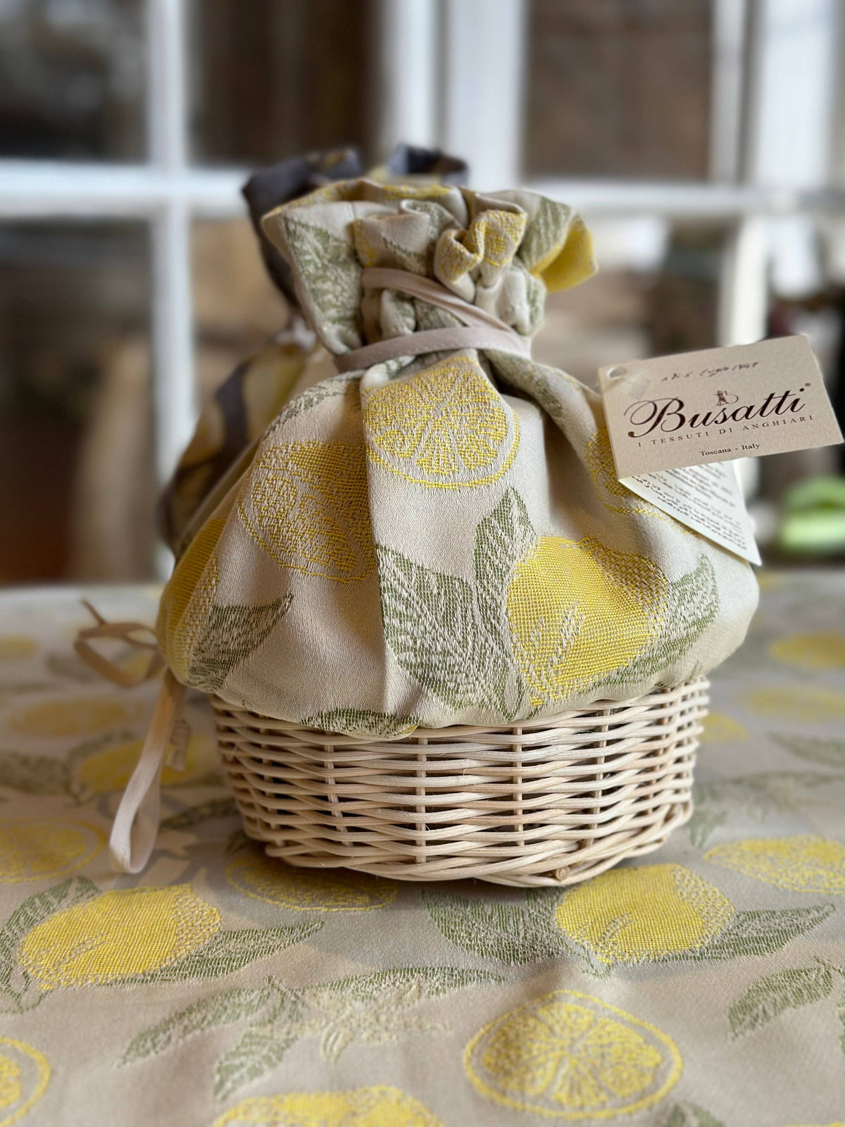 Wicker basket with a fabric cover featuring lemon design, on a matching tablecloth.
