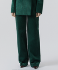 A person wearing a dark green velvet-like blazer and matching wide-leg trousers, shown from the shoulders down against a light gray studio background.