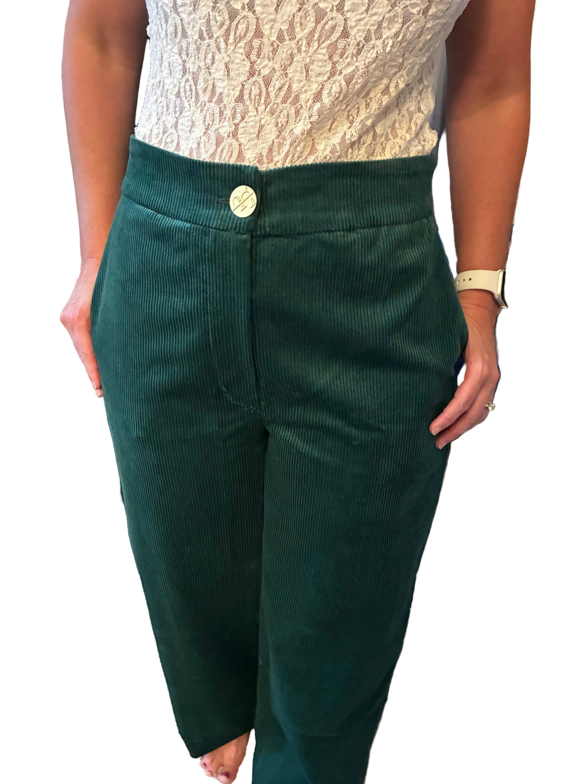 A person wearing dark green corduroy pants with a single light-colored button at the waist, paired with a cream lace top, standing in a clothing store.